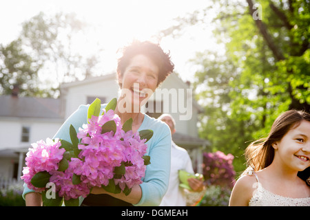 Familienfest. Eine Frau trägt einen großen Blumenstrauß Rhododendron, lächelt breit. Stockfoto