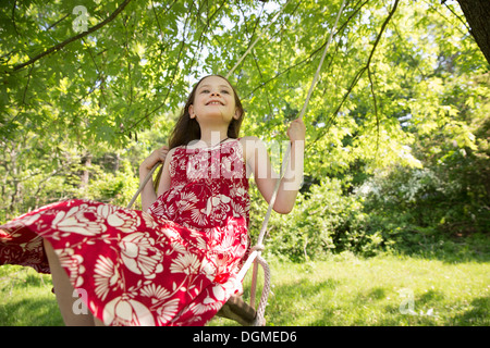 Sommer. Ein Mädchen in einem Sommerkleid auf einer Schaukel Aussetzung von den Ästen eines Baumes. Stockfoto