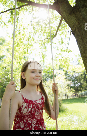 Sommer. Ein Mädchen in einem Sommerkleid auf einer Schaukel in einem Obstgarten. Stockfoto