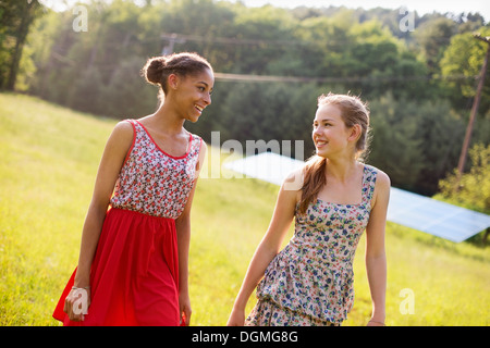 Zwei junge Mädchen auf dem Hof, im Freien. Ein großes Solar-Panel im Feld dahinter. Stockfoto