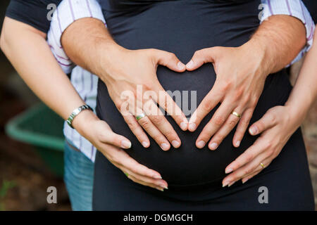 Mann und schwangere Frau bilden die Form eines Herzens mit ihren Händen auf den Bauch Stockfoto