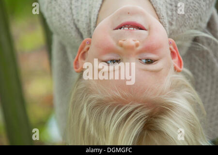 Mädchen, 4 Jahre alt, kopfüber hängend auf einem Holzzaun Stockfoto