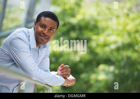 Sommer. Business-Leute. Ein Mann stützte sich auf einen erholsamen Geländer. Weg vom Rasterfeld. Stockfoto