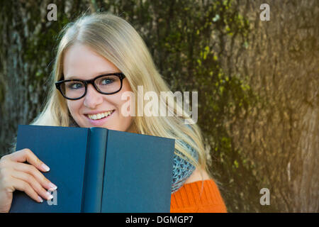 Junge Frau mit Brille schauen über den Rand eines Buches Stockfoto