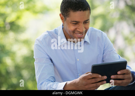 Sommer. Business-Leute. Ein Mann sitzt mit einem digital-Tablette, in Kontakt zu bleiben. Stockfoto