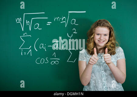 Schulmädchen, steht man vor einer Schultafel mit mathematischen Formeln, so dass eine Daumen-hoch-Geste, Deutschland Stockfoto