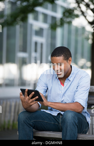 Sommer. Ein Mann sitzt auf einer Bank mit einem digitalen Tablet. Stockfoto