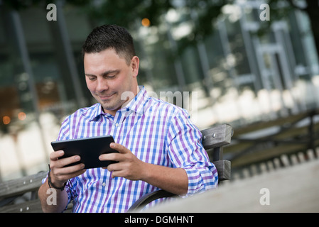 Sommer in der Stadt. Ein Mann sitzt auf einer Bank mit einem digitalen Tablet. Stockfoto