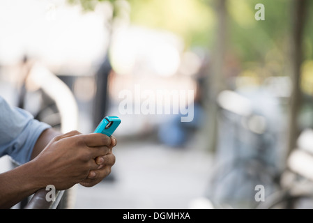 Sommer in der Stadt. Ein Mann sitzt auf einer Bank mit einem Smartphone. Stockfoto