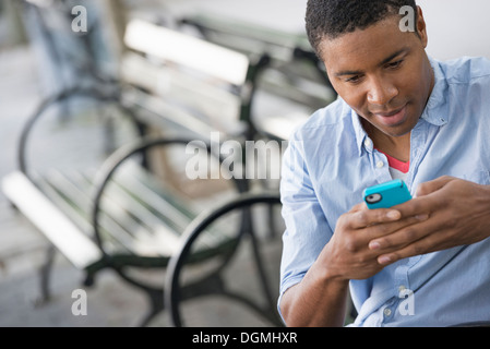 Sommer in der Stadt. Ein Mann sitzt auf einer Bank mit einem Smartphone. Stockfoto