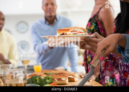 Ein informelles Büro-Ereignis. Menschen, die Ausgabe von Platten von Lebensmitteln über ein Buffet-Tisch. Stockfoto