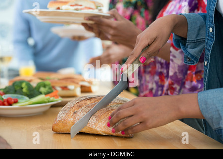 Ein informelles Büro-Ereignis. Menschen, die Ausgabe von Platten von Lebensmitteln über ein Buffet-Tisch. Stockfoto