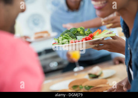 Ein informelles Büro-Ereignis. Menschen, die Ausgabe von Platten von Lebensmitteln über ein Buffet-Tisch. Stockfoto