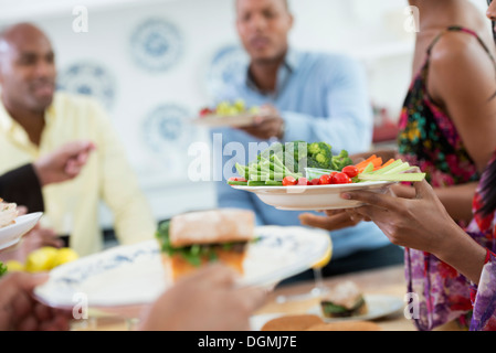 Ein informelles Büro-Ereignis. Menschen, die Ausgabe von Platten von Lebensmitteln über ein Buffet-Tisch. Stockfoto