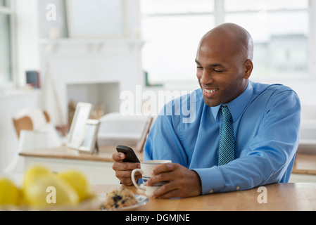 Ein Mann in einem blauen Shirt, sitzen an einem Frühstück bar mit einem Smartphone. Stockfoto