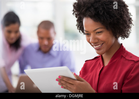 Büroalltag. Zwei Personen im Hintergrund und eine junge Frau, die mit einem digitalen Tablet. Stockfoto