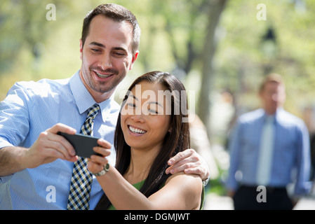 Ein paar mit einem Smartphone, nebeneinander. Ein Mann im Hintergrund. Stockfoto