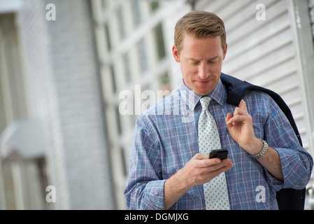 Ein Mann mit seiner Jacke, die über die Schulter geschlungen überprüft sein Telefon. Stockfoto