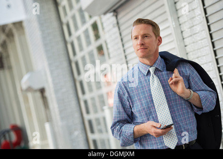 Ein Mann mit seiner Jacke, die über die Schulter geschlungen überprüft sein Telefon. Stockfoto