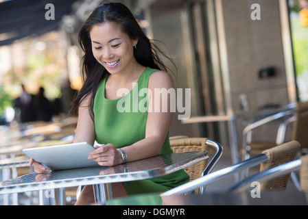 Eine Frau sitzt im Freien an einem Cafétisch mit einem digitalen Tablet.