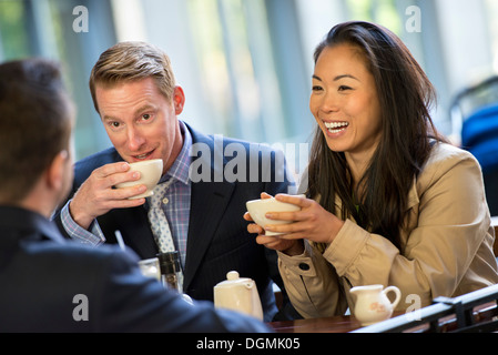 Eine Geschäftsfrau und zwei Geschäftsleute sitzen in einem Café, einer Tasse Kaffee. Stockfoto