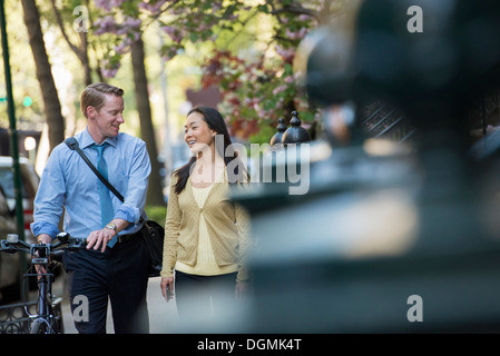 Ein Mann in ein Hemd und Krawatte ein Fahrrad schieben, und im Gespräch mit einer Frau. Stockfoto