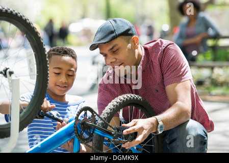 Eine Familie im Park an einem sonnigen Tag. Vater und Sohn ein Fahrrad reparieren. Stockfoto