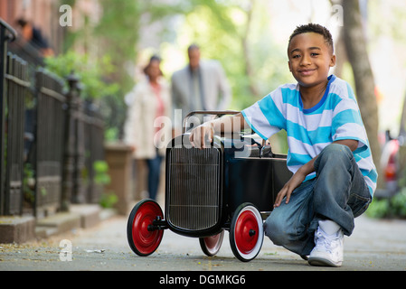 Ein kleiner Junge spielt mit einem alten altmodischen Spielzeugauto auf Rädern auf einer Stadtstraße. Ein paar auf der Suche auf. Stockfoto