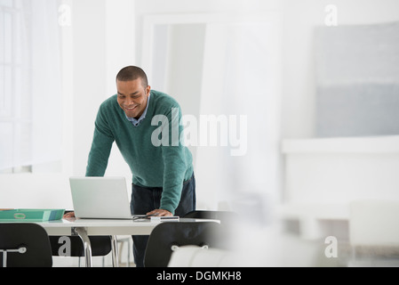 Geschäft. Ein Mann steht über einen Schreibtisch, lehnt sich nach unten, einen Laptop-Computer zu verwenden. Stockfoto