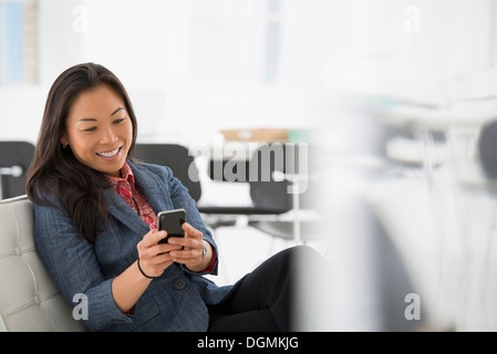 Geschäft. Eine Frau sitzt in einem bequemen Sessel, überprüfen ihr Smartphone für Nachrichten. Stockfoto