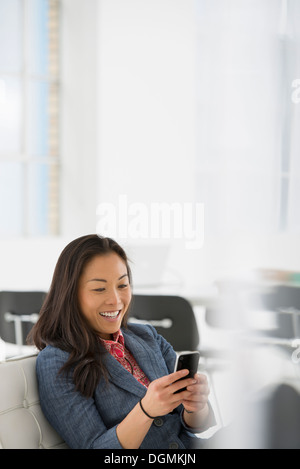 Geschäft. Eine Frau sitzt in einem bequemen Sessel, überprüfen ihr Smartphone für Nachrichten. Stockfoto