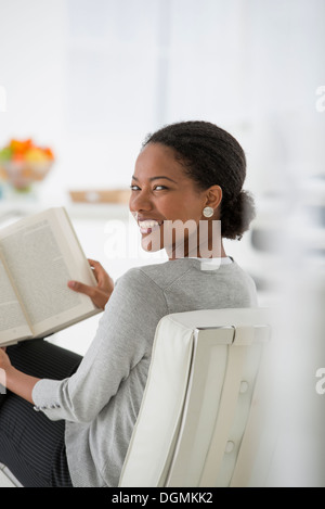 Geschäft. Eine Frau sitzt und liest ein Buch. Forschung oder Entspannung. Über die Schulter schauen und Lächeln auf den Lippen. Stockfoto