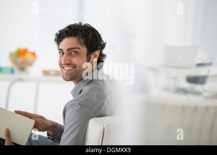 Geschäft. Ein Mann sitzt, der ein Buch in seinen Händen hält. Umdrehen und Lächeln auf den Lippen. Stockfoto