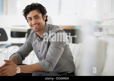 Geschäft. Ein Mann sitzt mit seinen Händen umklammert in entspannter Haltung. Lächelnd und nach vorne gelehnt. Stockfoto