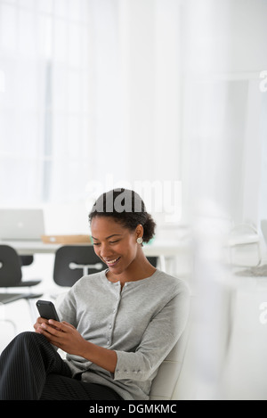 Geschäft. Eine Frau sitzt in einem bequemen Sessel, überprüfen ihr Smartphone für Nachrichten. Stockfoto