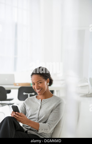 Geschäft. Eine Frau sitzt in einem bequemen Sessel, überprüfen ihr Smartphone für Nachrichten. Stockfoto