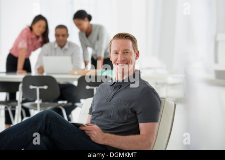 Geschäft. Vier Personen, ein Mann sitzt auf einem weichen Stuhl, und drei Personen gemeinsam an einem Laptop arbeiten. Stockfoto