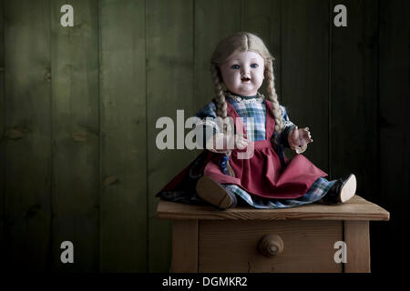 Antike Puppe sitzt auf einer kleinen Kommode Stockfoto