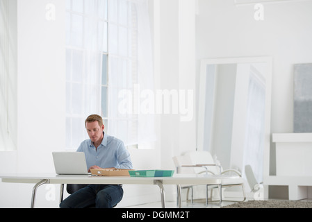 Geschäft. Ein Mann sitzt an einem Schreibtisch mit einem Laptop. Stockfoto