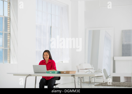 Arbeitsumfeld, hell und luftig. Eine Frau sitzt mit einem Laptop. Stockfoto