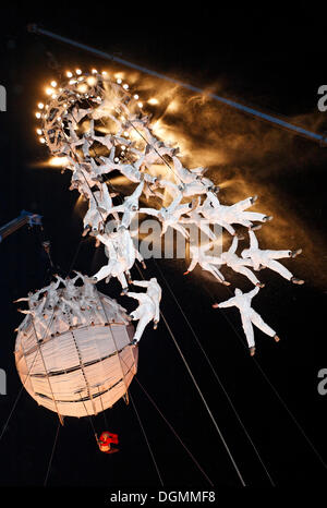 Weiß gekleidete Trapezkünstler und Globus schweben in den Himmel, globale Rheingold, Open-Air-Theater von La Fura Dels Baus Stockfoto