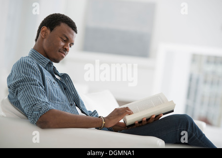 Ein helles weißes Zimmer Interieur. Ein Mann sitzt ein Buch zu lesen. Stockfoto