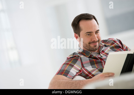 Ein helles weißes Zimmer Interieur. Ein Mann sitzt ein Buch zu lesen. Stockfoto