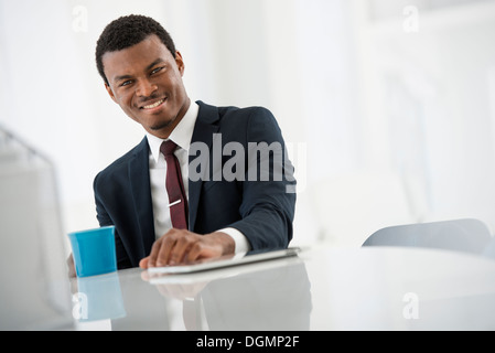 Büroeinrichtung. Ein Mann in einem Anzug mit einer Tasse Kaffee. Ein digital-Tablette auf dem Tisch. Stockfoto