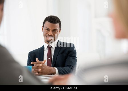 Büro innen drei Leute sitzen herum und Tabelle Geschäftstreffen Mann im Anzug Tasse Kaffee-digital-Tablette auf Tisch. Stockfoto