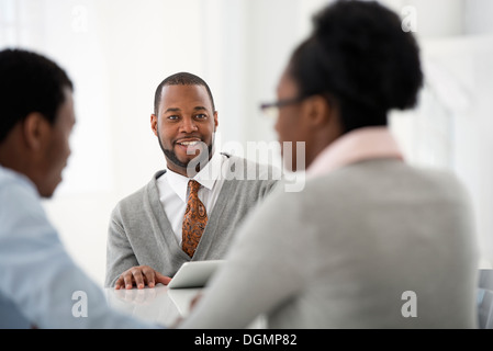 Büroeinrichtung. Drei Personen sitzen um einen Tisch bei einem Geschäftstreffen. Stockfoto