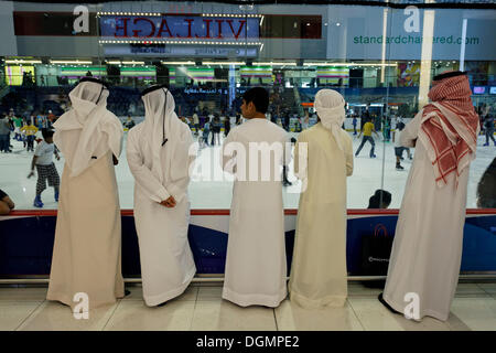 Araber, die traditionellen weißen Dischdascha tragen Roben beobachten Eisläufern, Dubai Ice Rink, Dubai Mall, Vereinigte Arabische Emirate Stockfoto