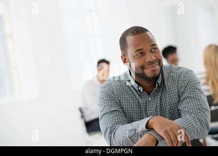 Büroeinrichtung. Ein Mann sitzt separat aus einer Gruppe von Menschen an einem Tisch sitzen. Ein Business-Meeting. Stockfoto