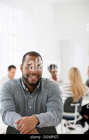 Büroeinrichtung. Ein Mann sitzt separat aus einer Gruppe von Menschen an einem Tisch sitzen. Ein Business-Meeting. Stockfoto