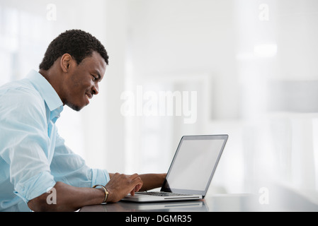 Büroeinrichtung. Ein Mann sitzt an einem Tisch mit einem Laptopcomputer. Stockfoto